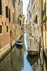 Parked boats in small side canal in city of Venice, Italy