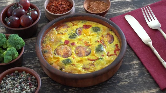 Ceramic bowl with vegetable frittata, simple vegetarian food. Frittata with egg, tomato, pepper, onion, broccoli and cheese on wooden table, close up. Italian egg omelette, rotates