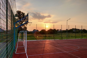 Outdoors mini football and basketball court with ball gate and basket surrounded with high protective fence.