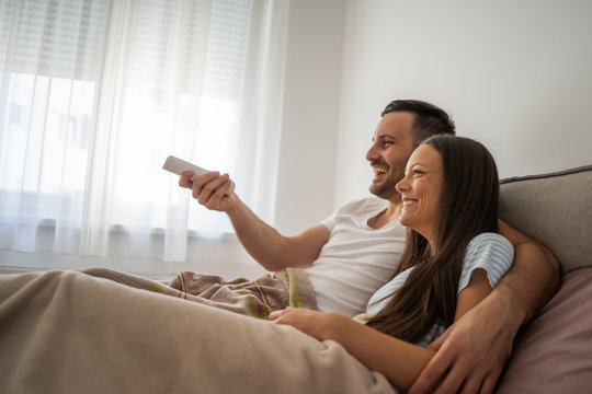 Young Couple Is Watching Tv In Their Bedroom.