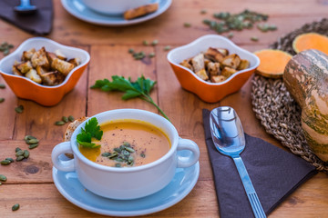 Vegetarian autumn pumpkin cream soup with bread croutons. Wooden table prepared for two people