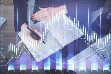 Forex chart hologram on hand taking notes background. Concept of analysis. Multi exposure