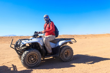 Fototapeta na wymiar Young man in safari trip through egyptian desert driving ATV. Quad bikes safari in the desert near Hurghada, Egypt