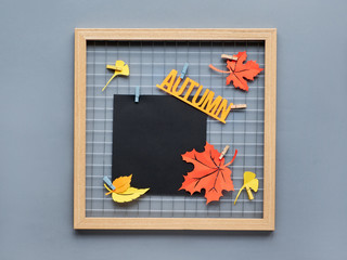 Photo grid board with red, orange and yellow paper Autumn leaves and text "Autumn" on pegs