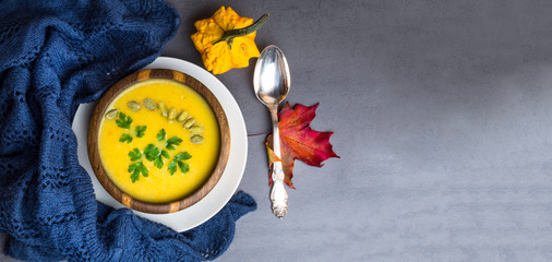 Vegetarian autumn pumpkin cream soup with seeds, parsley, in wooden bowl, autumn leaves and decorative pumpkins Top view