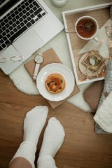 Toned photo. Autumn decor. Women's legs in knitted socks, a laptop, a mug of hot tea, a bun, candles. Cozy. Autumn.