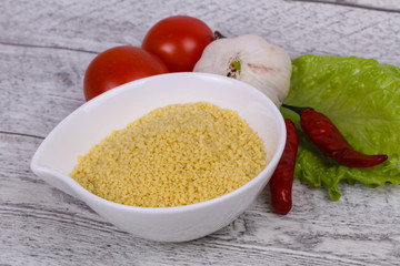 Raw couscous in the bowl served salad leaves, tomato and pepper
