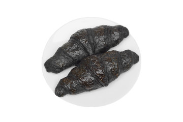 Black croissants on a white plate isolated