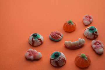 Halloween! Jelly candies in the form of eyes, brains, skulls, teeth with fangs, pumpkins in the lower right corner on a bright orange background. Copy space