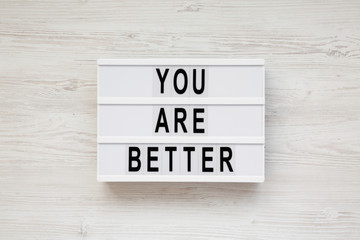 'You are better' words on a lightbox over white wooden background, top view. Overhead, from above. Flat lay.