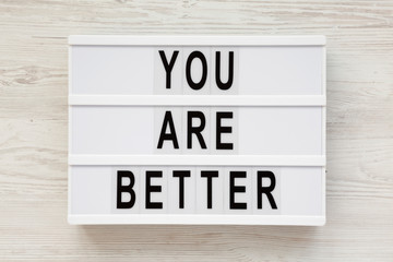 'You are better' words on a modern board over white wooden background, top view. Overhead, from above. Flat lay.