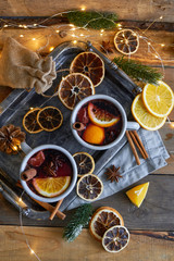 Christmas mulled wine in two rustic mugs with fruits and spices on wooden background