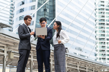 group of asian business people working and discussing something positive with his mature colleague and using a laptop at outdoor in the capital