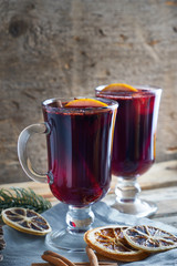 hot mulled wine in two glasses with fruits and spices on wooden background