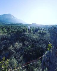 A man is walking along a stretched sling. Highline in the mountains. Man catches balance....