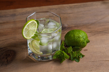 Summer cocktail mojito in glass, sliced lime and mint on wooden background..