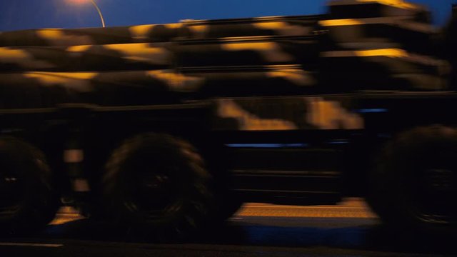 A convoy of military equipment rides through the city at night with headlights on