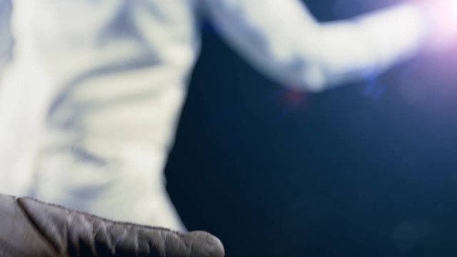 Sport girl fencer puts on epee glove before competition in fencing hall with light background.