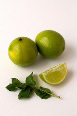 green limes and fresh leaves of mint on white background. vertical frame