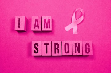 pink ribbon shape and the word - I am strong - on cubes on a pink background. October National Breast Cancer Awareness Month symbol