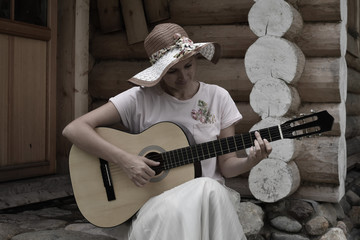 A girl plays the guitar on the porch of a wooden house.