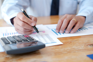 Businessman analyzing investment charts and pressing calculator buttons over documents. Accounting Concept.