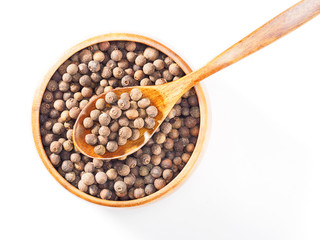 Allspice (Jamaica pepper) in wooden cup and spoon diagonally on white background