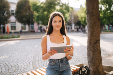 Beautiful girl use tablet outside. Female sitting on the bench. Hot summer day