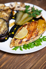 Delicious grilled chicken fillet and eggplant on a plate. Dark wooden table as a background