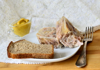 Jelly with meat, beef jelly, traditional Russian dish, serving on a plate, mustard, bread, tomatoes. Side light. Close-up.
