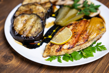 Delicious grilled chicken fillet and eggplant on a plate. Dark wooden table as a background