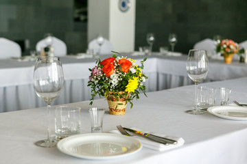 A closeup of restaurant table set with colourful flower bouquet in wicker wase