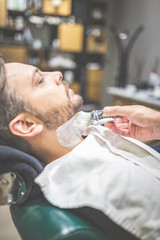 Obraz na płótnie Canvas Professional hairdresser applying shaving foam on client skin in barbershop.