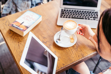 Woman at work or study in a cafe. She drinks coffee and do business using her laptop. Copy space