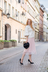 Cute cheerful caucasian woman walking on european street. She wear stylish outfit.