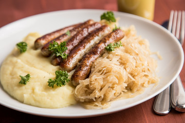 Kleine Bayrische Nürnberger Rostbratwürste mit Sauerkraut, Kartoffelpüree und Senf auf Holz Tisch Hintergrund