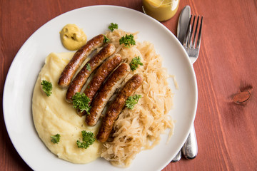Kleine Bayrische Nürnberger Rostbratwürste mit Sauerkraut, Kartoffelpüree und Senf auf Holz Tisch Hintergrund