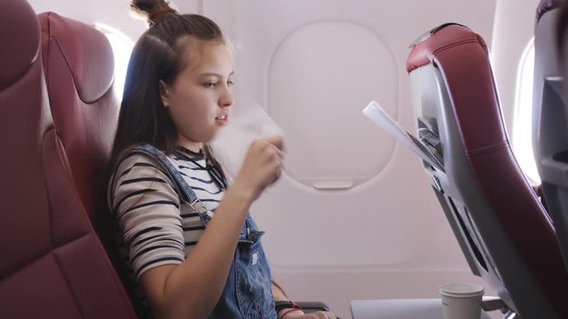 Teen girl on the plane vomited in a paper bag. Traveler in a flying aircraft has nauseous. Nausea passenger in a flying airplane. Turbulence on the plane.