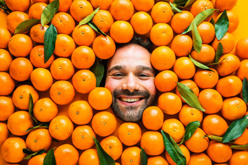 Man with ripe oranges or clementines Face of grimacing man in tangerines area