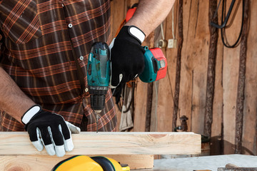 A man carpenter twists a screw into a tree with an electric screwdriver, male hands with a...