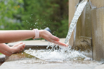 A closeup of womans hands, catching water stream from the fountain
