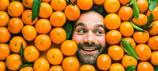 Man with ripe oranges or clementines Face of grimacing man in tangerines area