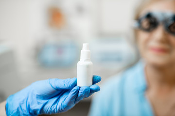 Nurse in medical gloves holding white bottles or droppers with eye medicine with senior patient on the background, close-up view, bottles with blank space