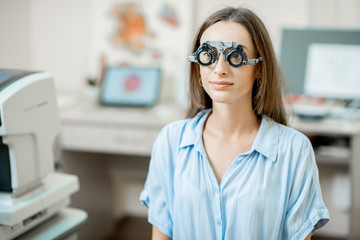 Fototapeta premium Young woman checking vision with eye test glasses during a medical examination at the ophthalmological office