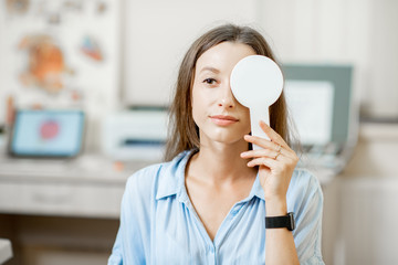 Young woman checking vision covering one eye with an ophthalmic scapula during a medical examination at the ophthalmological office © rh2010