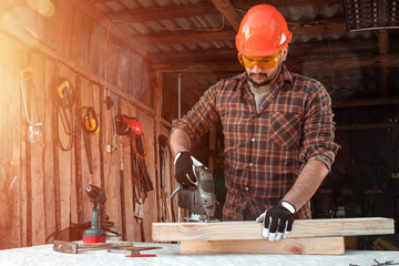 A man carpenter cuts a wooden beam using an electric jigsaw, male hands with an electric jigsaw closeup. Work with wood.
