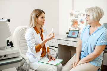 Obraz premium Senior woman patient talking with female ophthalmologist during a medical consultation at the ophthalmologic office. Doctor offering eye medcine for a patient