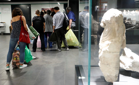 People holding bags full of plastic bottles queue in front of a recycling machine in San Giovanni metro station in Rome