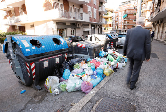 Residents walk along piles of garbage lying in front of rubbish bins in Rome