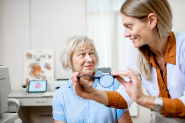Fototapeta premium Ophthalmologist offering eyeglasses for vision to a senior woman patient during a medical consultation in the office